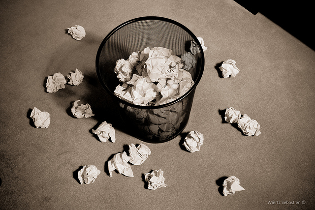 Poubelle de bureau remplie de papiers froissés, des boules tombées autour.