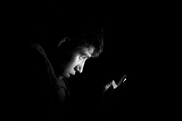 Joueur obsessionnel dans le noir éclairé par son smartphone.