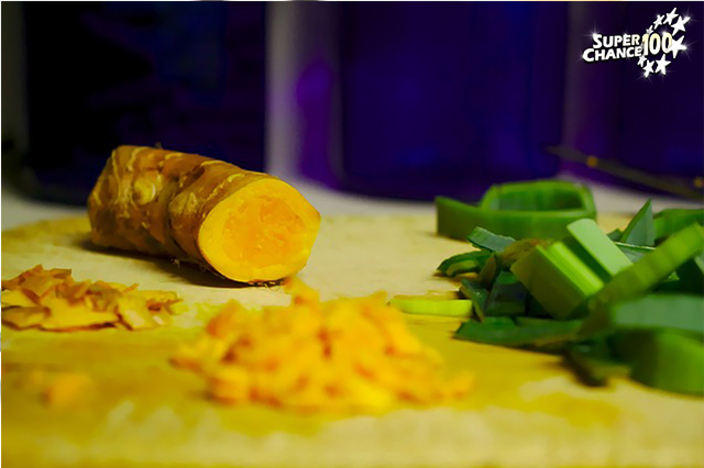 Rhizome de curcuma coupé en morceaux sur une planche en bois.